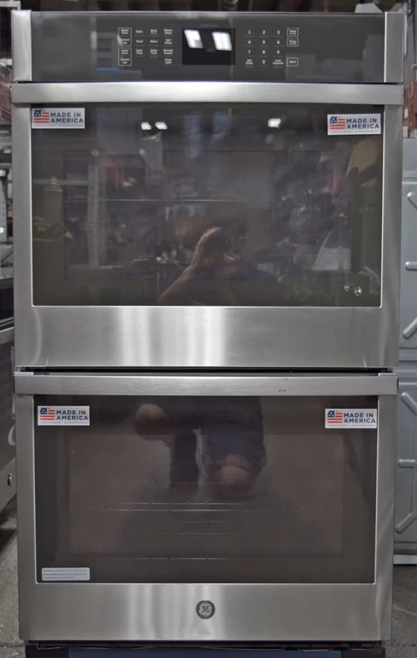A full shot of a brand new GE JTD3000SNSS 30-Inch Built-In Double Wall Oven with a photographer's reflection on its glass door.