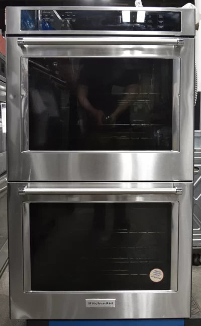 A front view of a brand new KitchenAid KODE500ESS 30′′ Double Electric Wall Oven with Self-Cleaning Glass Door, showing a photographer holding a camera.
