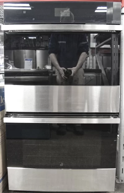 A front shot of a brand new Jenn-Air Noir JJW2830IM 30-Inch Electric Double Wall Oven with MultiMode Convection System with the photographer's reflection on its glass door.